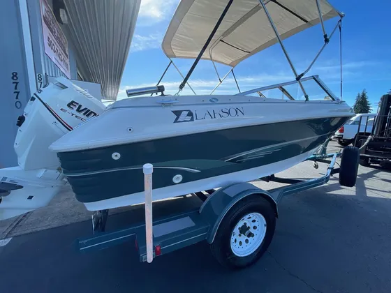Cream and green Larson bowrider with a bimini top on a trailer in the lot, blue sky behind