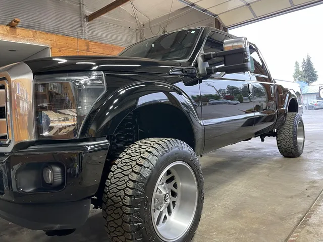 Black lifted pickup with tow mirrors and large chrome wheels inside the shop bay