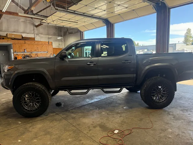 Lifted dark gray crew cab pickup with large off-road tires and side steps in the shop bay