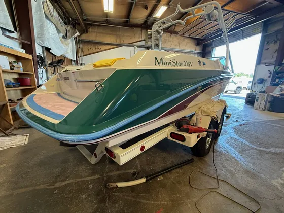 Green and cream MariStar 225V boat in the shop with blue tape on the edge and a polisher on the trailer