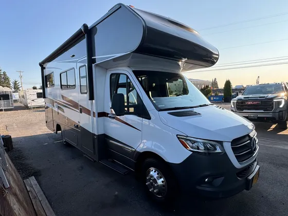 White and brown Class C motorhome on a Mercedes Sprinter chassis parked in the lot at sunset