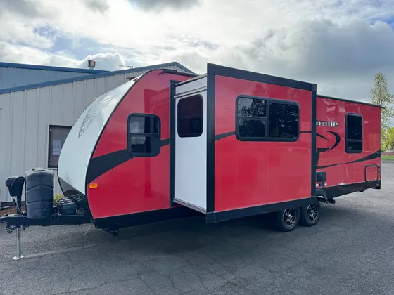 Red and black Minnie travel trailer with the slide-out extended, parked in the lot
