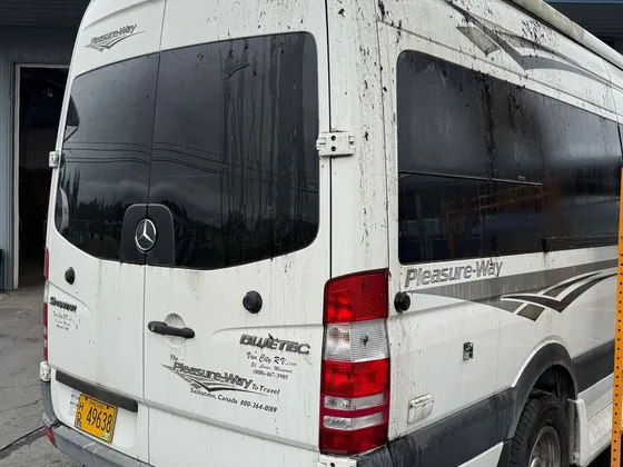 Rear of a white Sprinter camper van covered in mud splatter, parked wet outside the shop