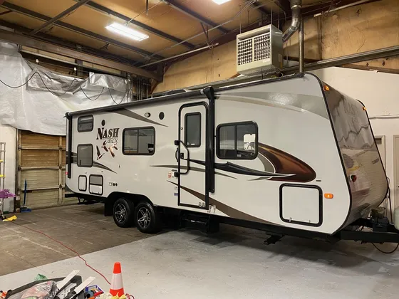White and tan Nash DLX travel trailer parked inside the shop with its door side facing the camera