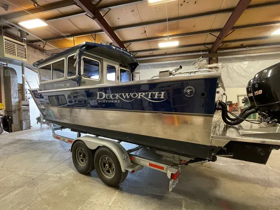Navy and aluminum Duckworth 26 Offshore with twin outboards on a trailer inside the shop