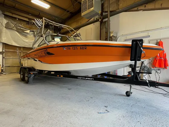 Orange and white Centurion wake boat with a tower on a black trailer inside the shop