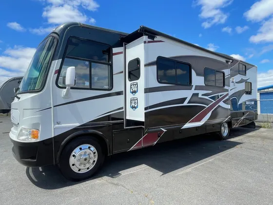 White and black Outlaw Class A motorhome with maroon graphics parked in a lot under a blue sky