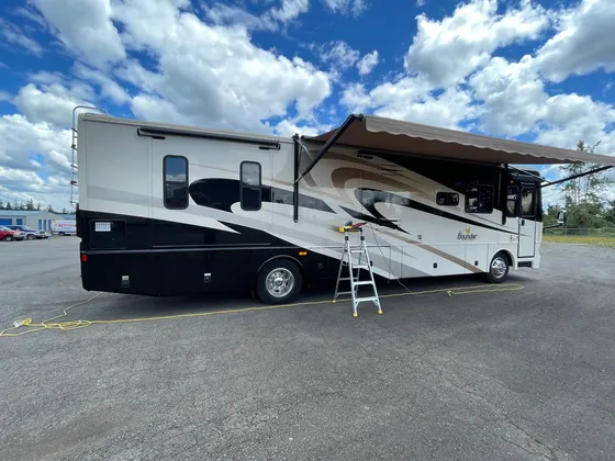 Black and cream Bounder motorhome with the awning out, a step ladder and a polisher against the side wall