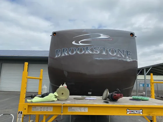 Dull brown front cap of a Brookstone fifth wheel with polishers and pads laid out on a scaffold platform