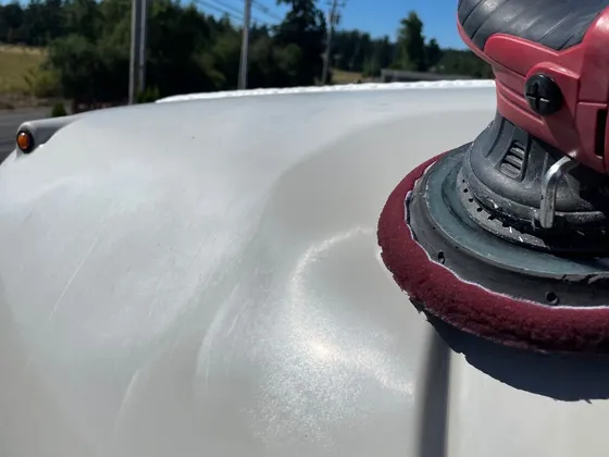 Dual-action polisher with a maroon pad sitting on the dull front roof cap of an RV