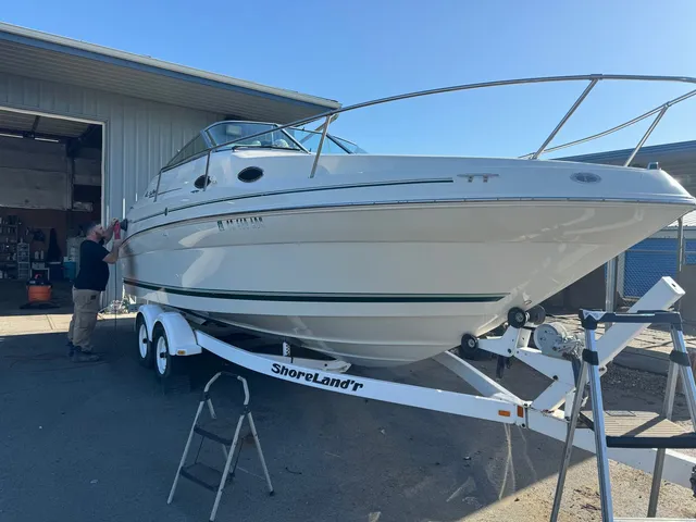 Man working a polisher on the hull of a cream cabin cruiser sitting on its trailer outside the shop