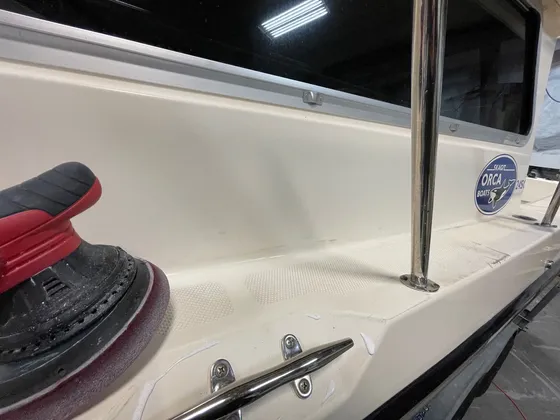 Orbital polisher with a red foam pad and dabs of compound on the cream cabin side of a Skagit Orca boat