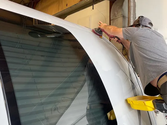 Man polishing the front cap of a white RV with an orbital polisher inside the shop