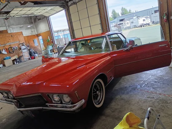 Red 1970s Buick Riviera with the driver door open inside a shop bay