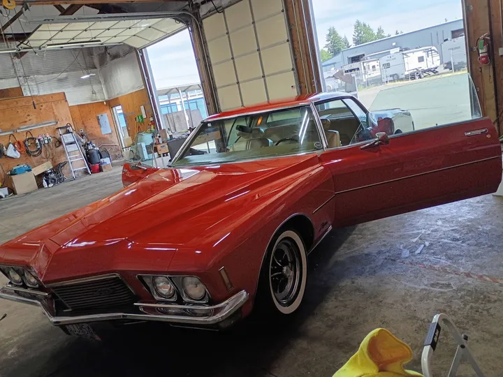 Red 1970s Buick Riviera with the driver door open inside a shop bay
