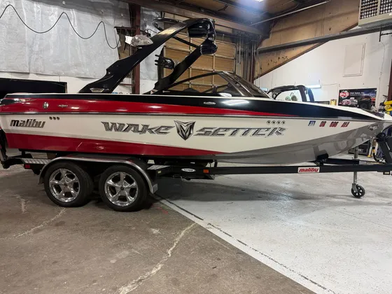Red, black and white Malibu Wakesetter wake boat with chrome wheels on its trailer inside the shop