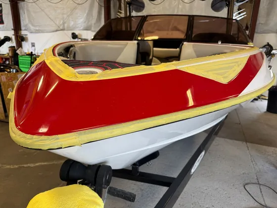 Red and white boat bow in the shop with yellow masking tape along the edges and a shiny red deck
