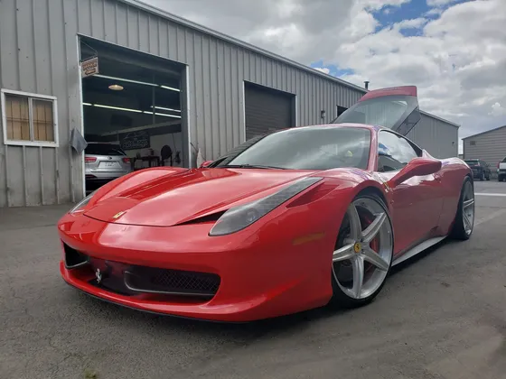 Red Ferrari 458 with the rear hood raised, parked outside the shop bay