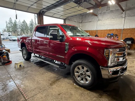 Red Ford Super Duty crew cab pickup with chrome wheels and running boards in the shop bay