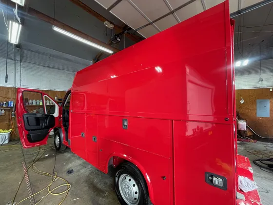 Red utility body van with the driver door open and hoses on the floor inside the shop