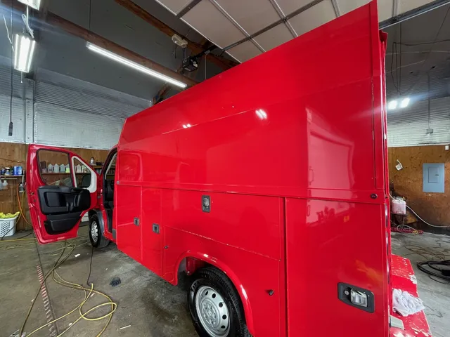Red utility body van with the driver door open and hoses on the floor inside the shop