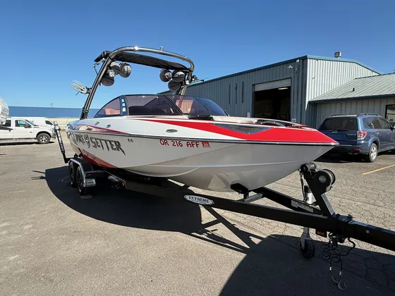 Red and white Malibu Wakesetter wake boat with a tower on its trailer in front of a metal shop building