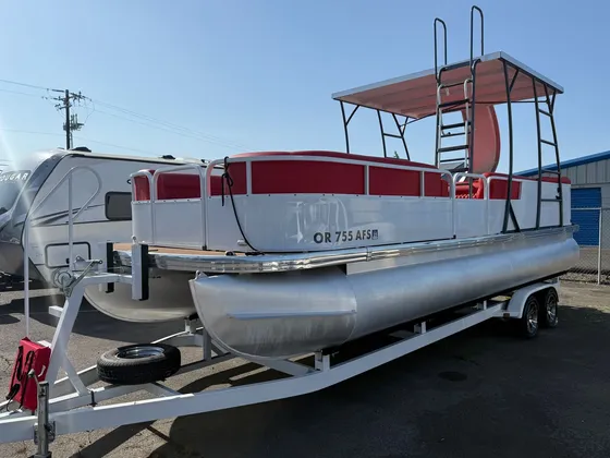 Silver pontoon boat with red seats, a canopy and a slide, sitting on its trailer outside