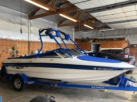 Cream and blue Reinell boat with a blue wake tower and blue covers on its trailer in the shop