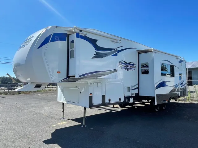 White Road Warrior fifth wheel with blue graphics parked on pavement under a clear blue sky