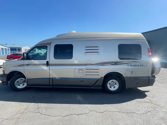 Tan Roadtrek 210 camper van parked in the sun on the lot, driver side
