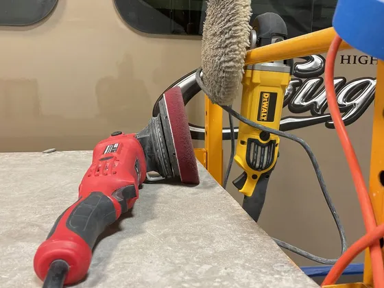 Red polisher, DeWalt buffer with a wool pad and blue tape on a scaffold in front of a tan RV wall