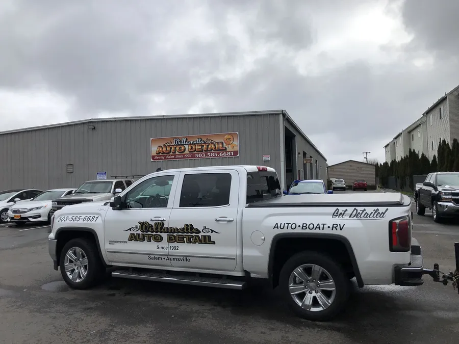 White crew-cab shop pickup with company lettering parked in front of the shop building