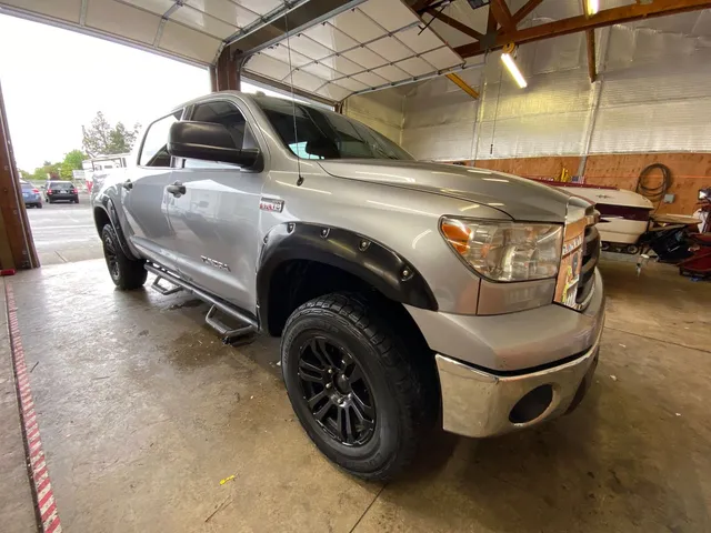 Silver Toyota Tundra crew cab with black wheels and fender flares parked in the shop bay