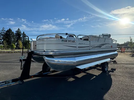 Sun Tracker pontoon boat on a trailer with bare aluminum tubes, parked in the lot in evening sun