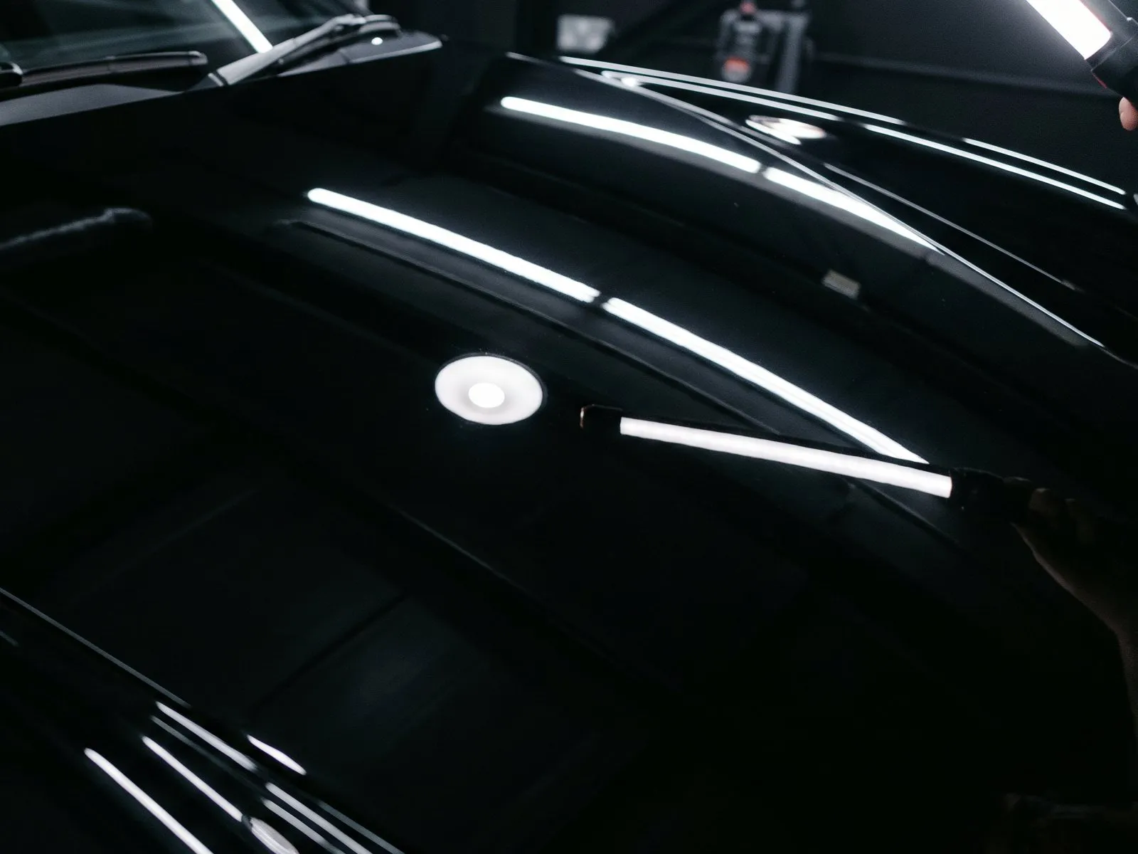 The same black hood after machine polishing, with a clean mirror reflection of the light
