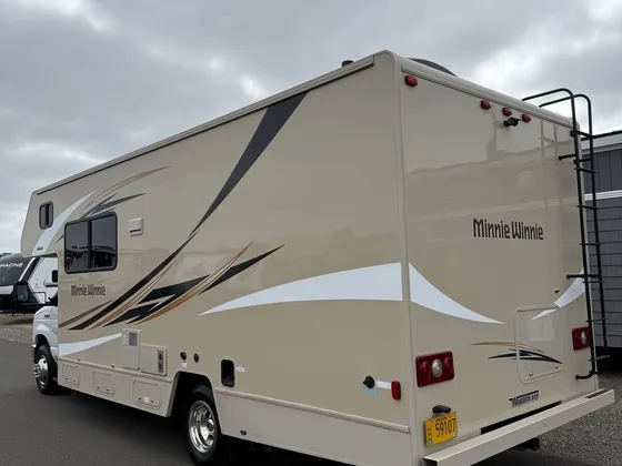 Tan Minnie Winnie class C motorhome seen from the rear driver side on a paved lot