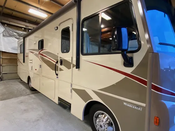 Tan and cream Winnebago Class A motorhome with red stripes parked inside the shop