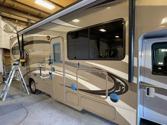 Side of a tan Four Winds motorhome with blue tape on the door and vents and a stepladder beside it