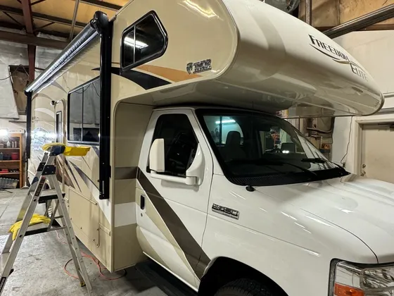 Cream and tan Thor Freedom Elite Class C motorhome in the shop bay with a stepladder at the side