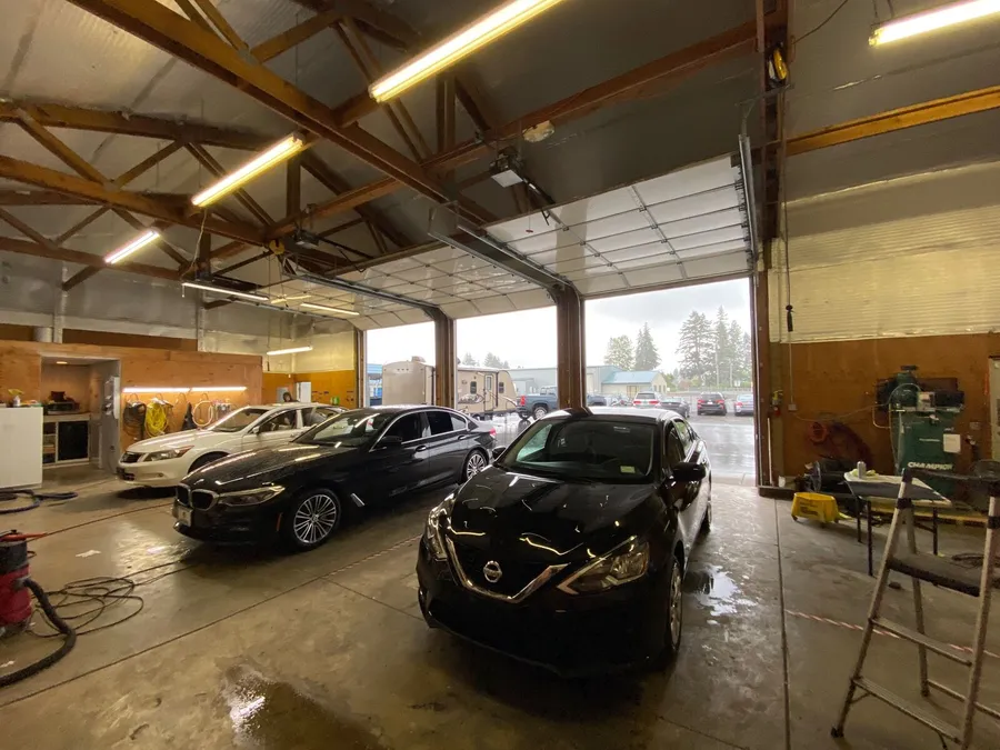 Black Nissan sedan, black BMW and white Honda parked in the shop bay with the big door open