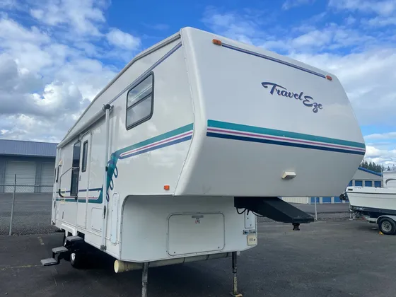 White Travel Eze fifth wheel with teal and purple stripes parked in a lot under a blue sky