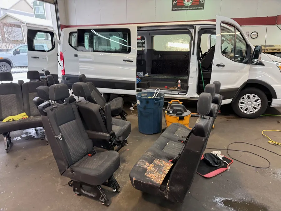 White passenger van in the shop with all the bench seats removed and lined up on the floor