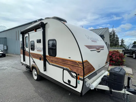 Cream Vintage Cruiser travel trailer with wood-look graphics and whitewall tires parked outside, door side