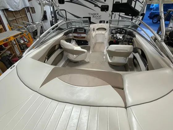 Tan and cream vinyl seats and helm inside a wake boat with a tower, parked in the shop