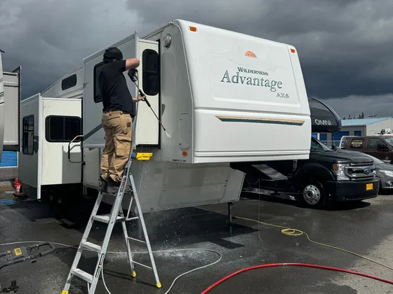 Man on a stepladder washing the side of a white Wilderness Advantage fifth wheel with a pressure wand