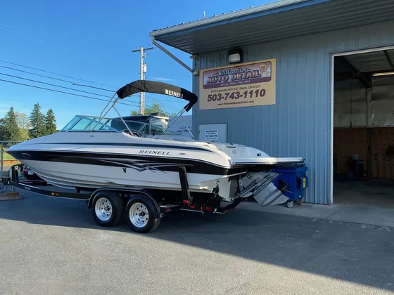 White boat with black graphics and a bimini top on a trailer in front of the shop, seen from the stern corner