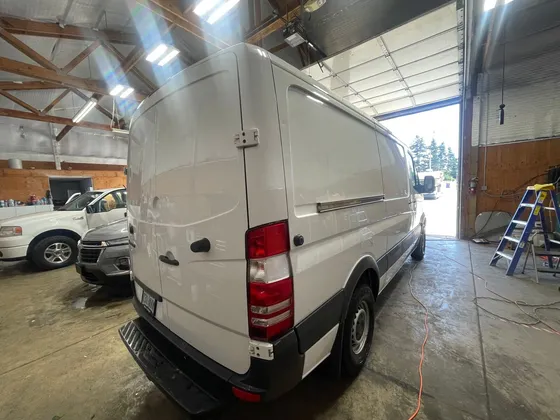 White cargo van seen from the rear driver side inside the shop bay