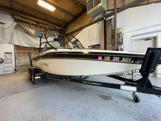 White Centurion ski boat with a tower on its trailer inside the shop, front three-quarter view
