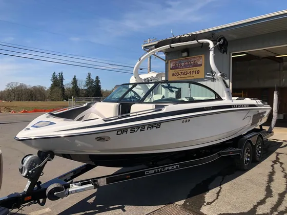 White and black Centurion wake boat with a tower on its trailer in front of the shop in sunshine