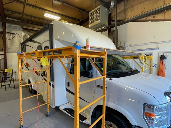 White Class C motorhome in the shop bay with a rolling scaffold set up along the side